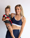 happy mum holding her toddler while wearing the nursing sports bra in navy and white 